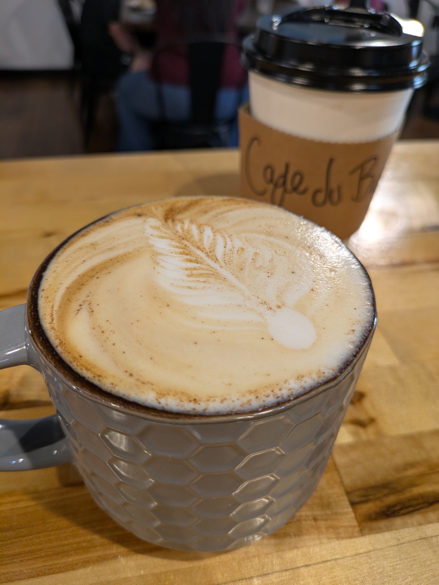 A latte with leaf art at Café Du Burg, next to a to-go cup