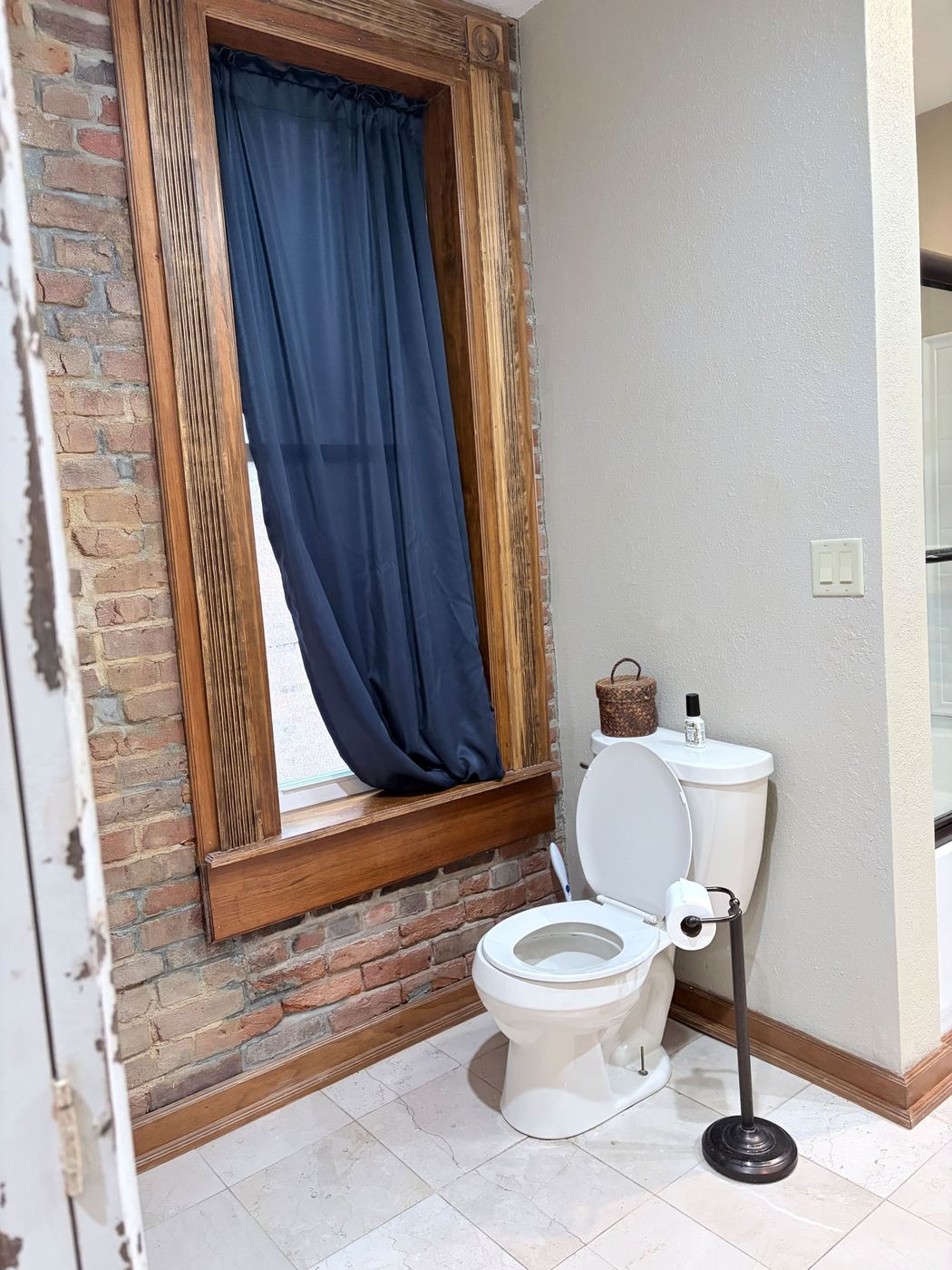 Bathroom with a tall wood-framed window and brick wall