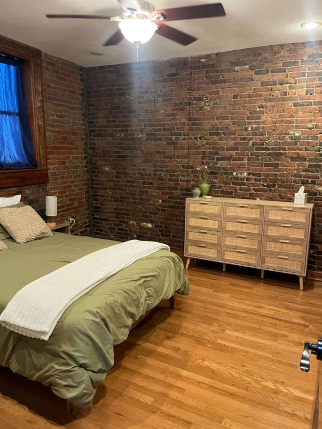 Bedroom with a rattan dresser against an exposed brick wall