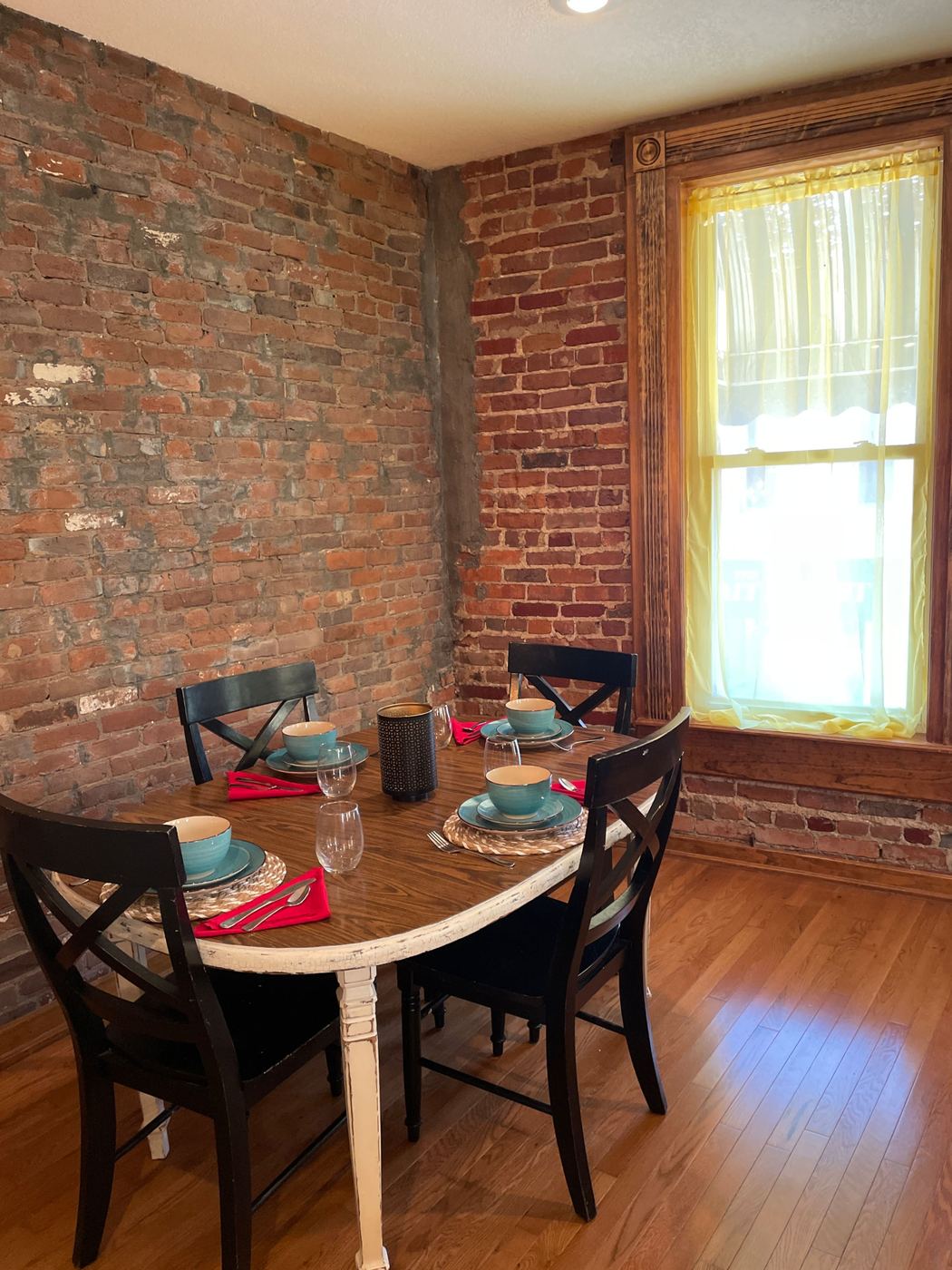 Dining table set for four beside a tall window and exposed brick