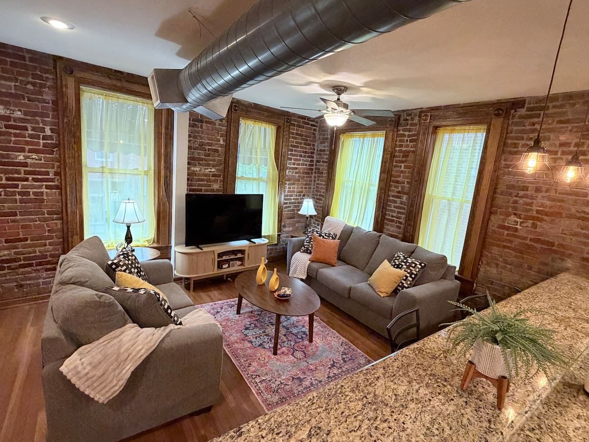 Living room with exposed brick, tall windows, and a modern gray sofa set